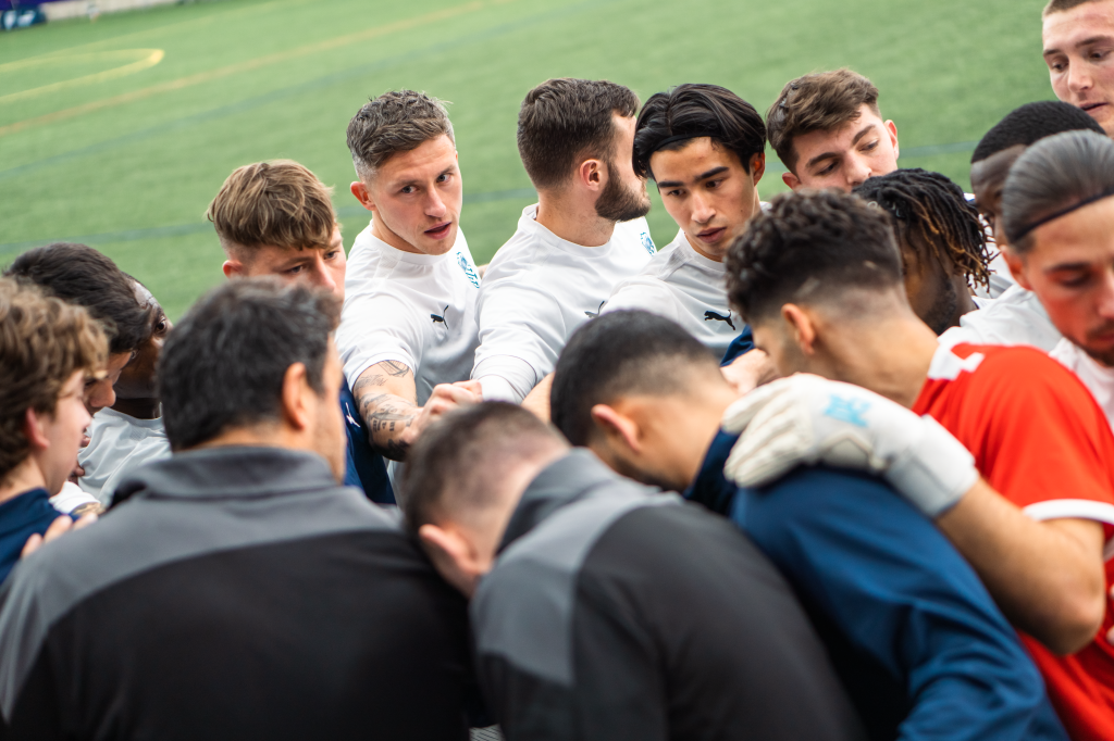 Hailstorm huddles ahead of their first preseason game vs. Harpos FC in the dome at Future Legends Complex. They all have their hands in the middle of the circle, looking intently toward head coach Eamon Zayed.