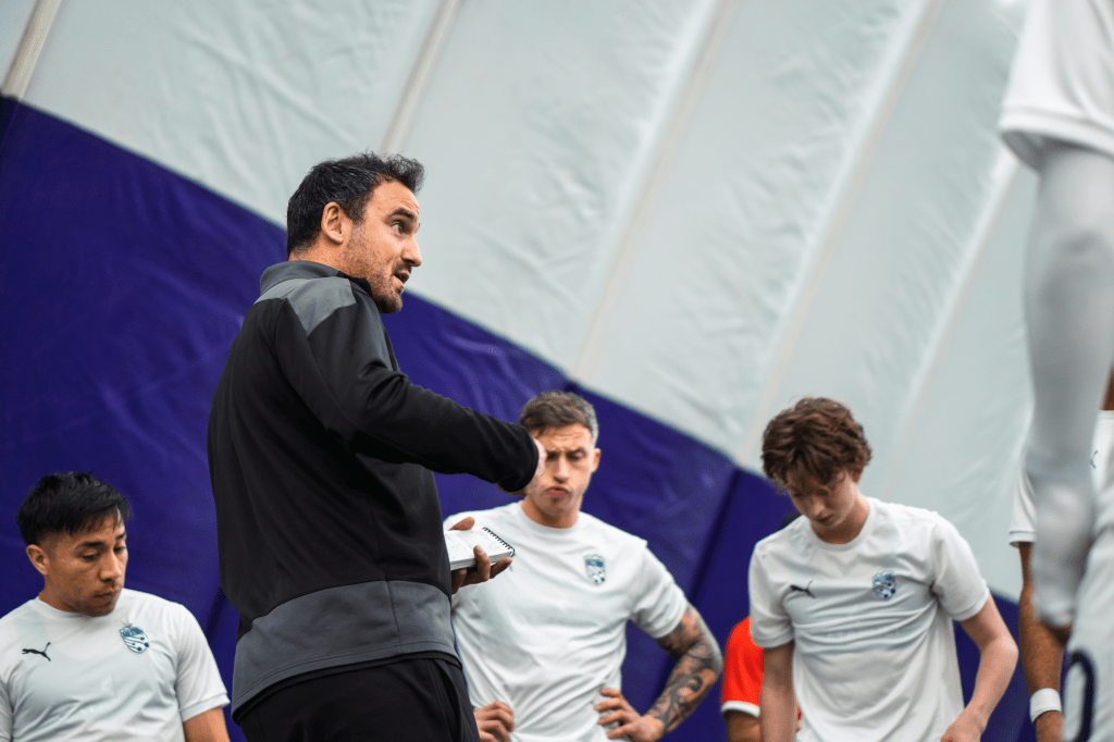 Head coach Eamon Zayed addresses his huddled Hailstorm team during halftime of a home preseason match vs. Harpos FC.