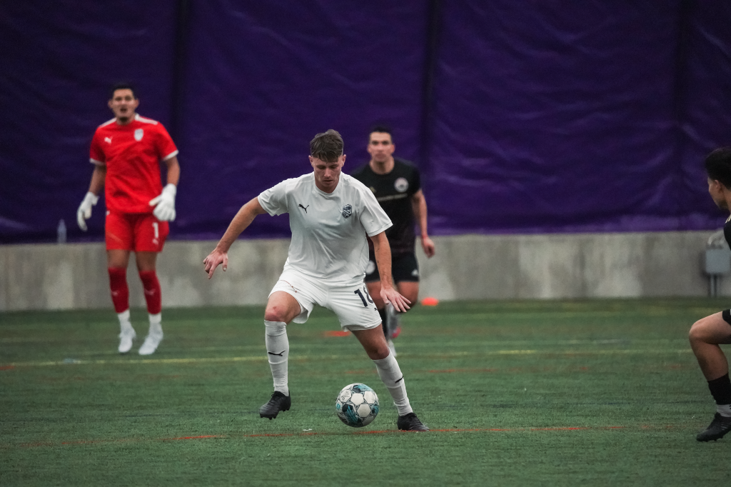 Jackson Dietrich starts making a move against an opposing defender. He is looking down at the ball, which is bouncing toward his right foot as he moves right.